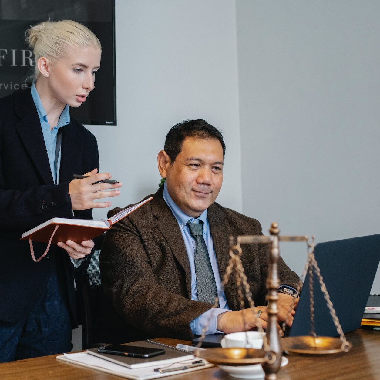 ethnic male lawyer showing document on laptop to young female colleague